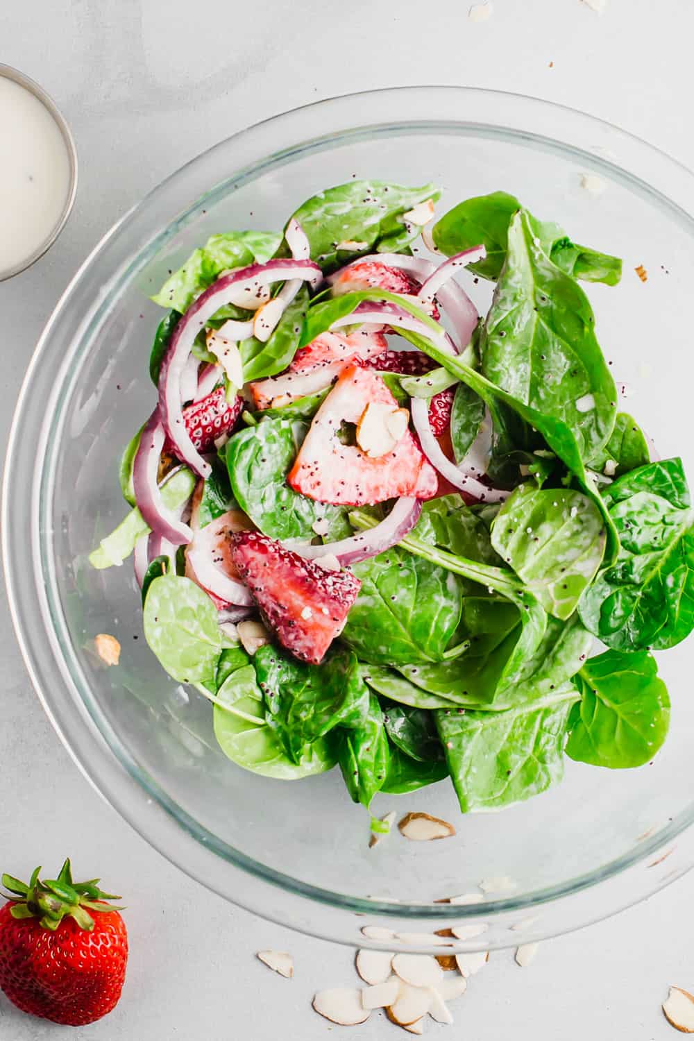 Spinach salad being mixed with poppyseed dressing in a clear bowl. 