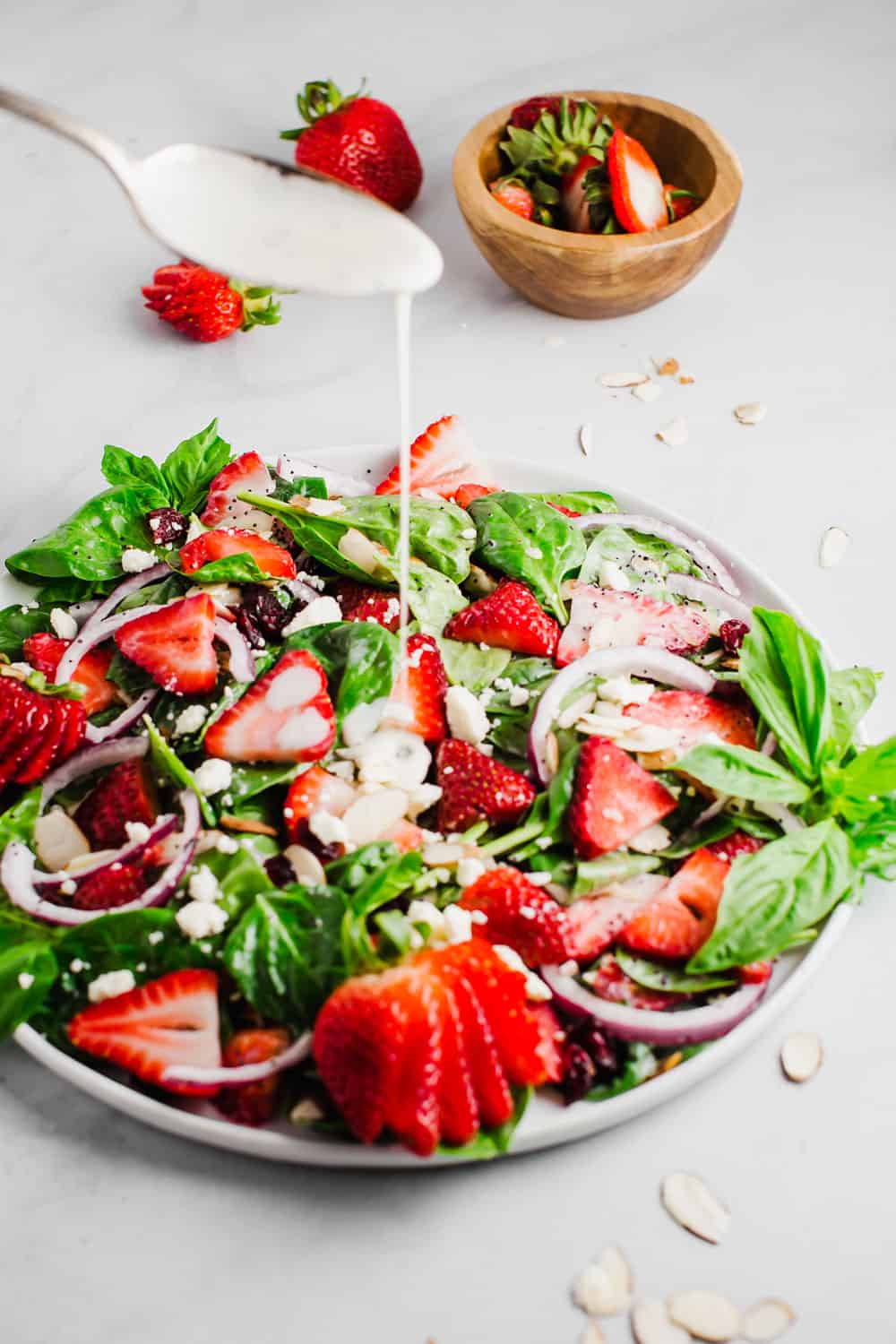 Poppyseed dressing being drizzled into a bowl of strawberry spinach salad. 