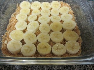 Sliced banana nicely aligned on crushed Nilla Wafer base in a clear baking pan. 