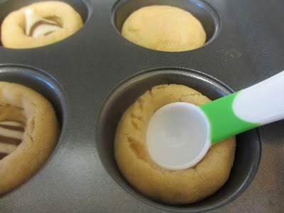 A spoon pushing down the dough in a muffin tin to make a space for the Hershey's Kisses. 