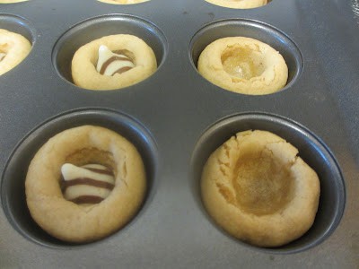 Close up photo fo muffin tin with dough with the Hershey's Kisses put in the center of the dough. 