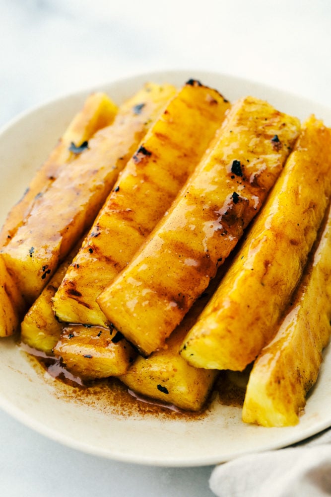 Lanzas de piña asadas en un plato blanco apilados uno encima del otro. 