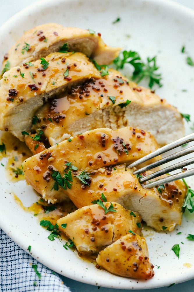 Baked honey butter chicken cut up on a white plate with a fork stabbing a piece of chicken. 