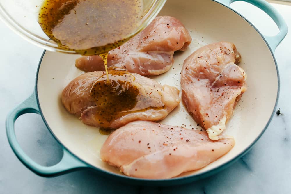 Chicken breasts in a pan being glazed with the whisked ingredients. 