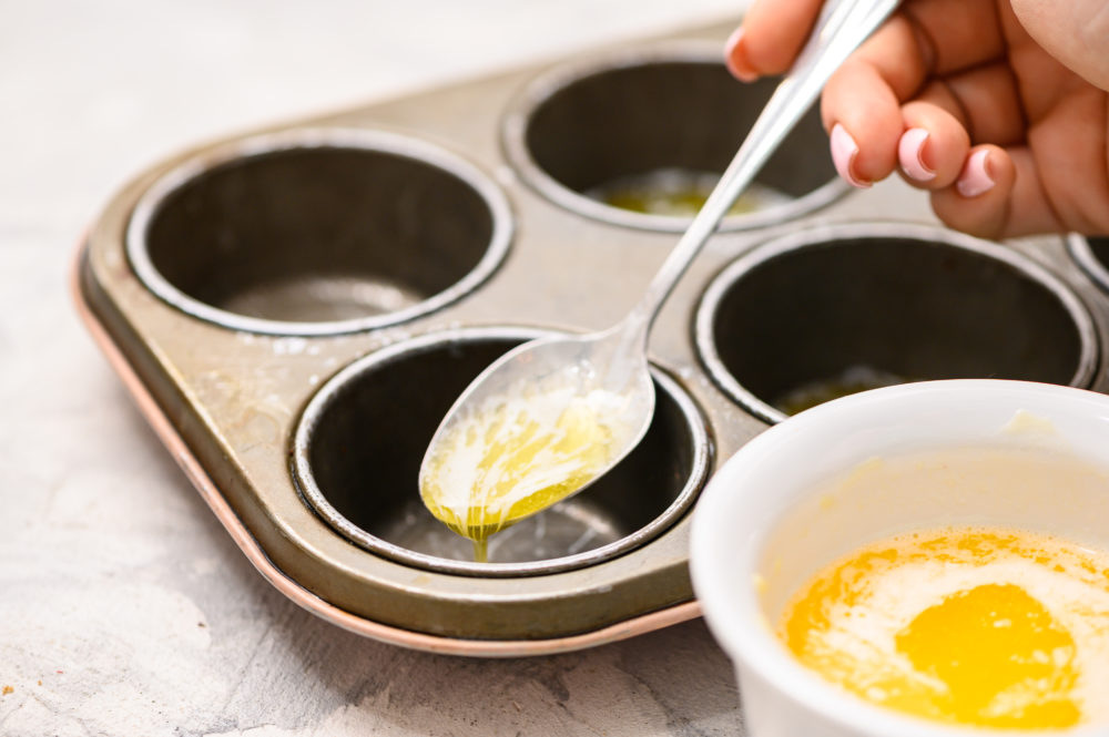 Adding butter by the spoon into the muffin tins. 