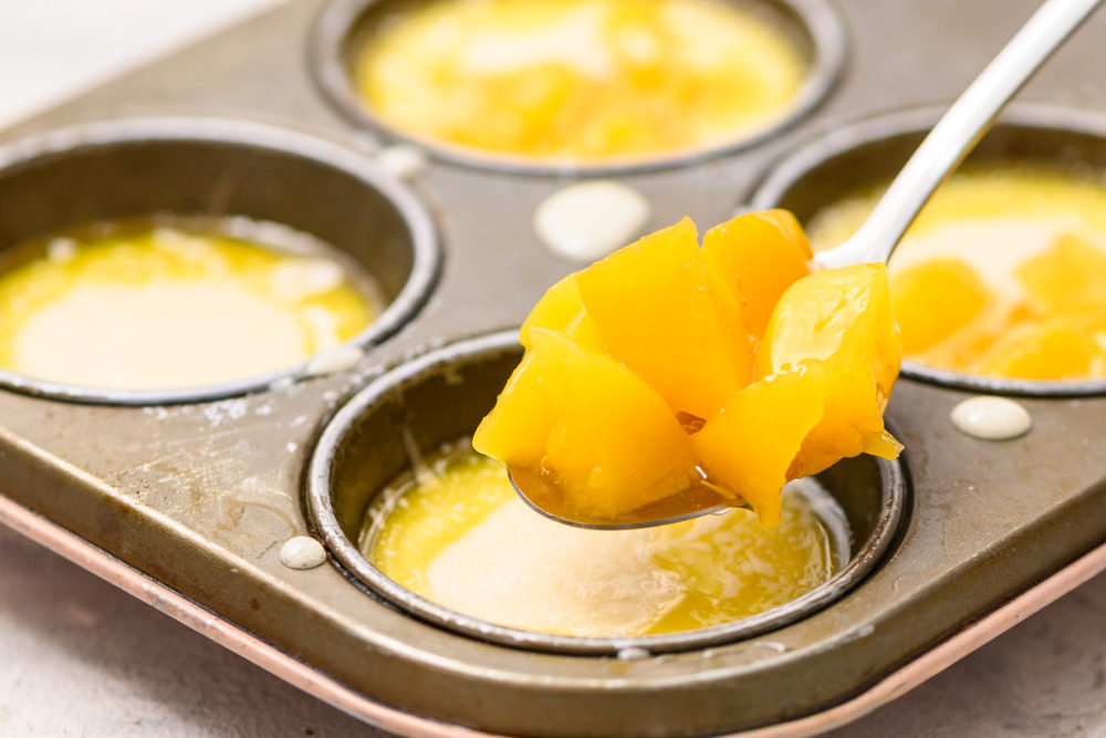 Adding peaches into the muffin tins with butter and cobbler mix. 