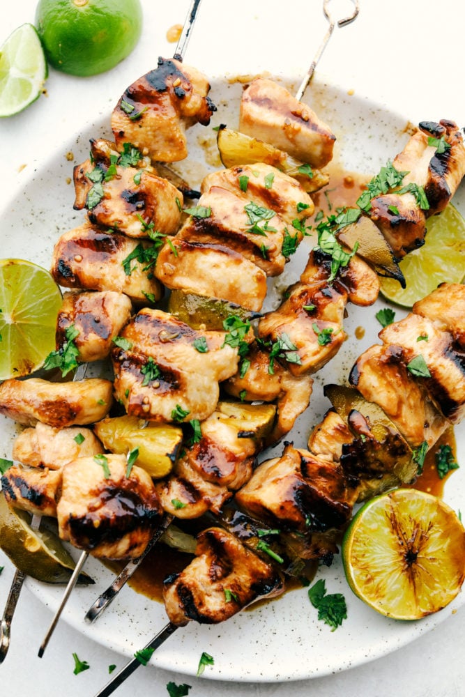 Grilled Key Lime Chicken on skewers on a white plate with fresh cut lemon on the side. 