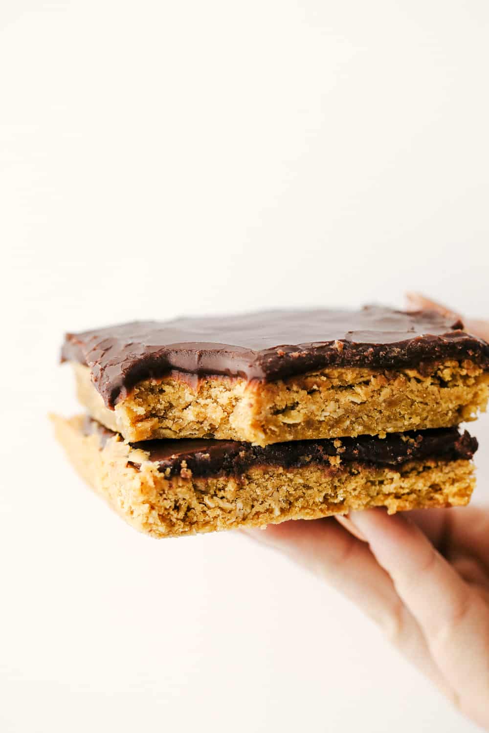 Two peanut butter bars stacked on top of each other being held by a hand. 