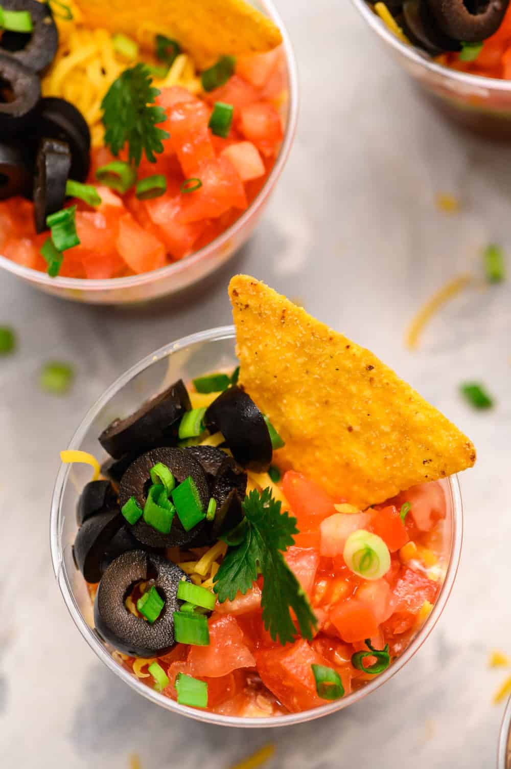 A photo of the individual cup with black olives, tomatoes, scallions and a chip. 