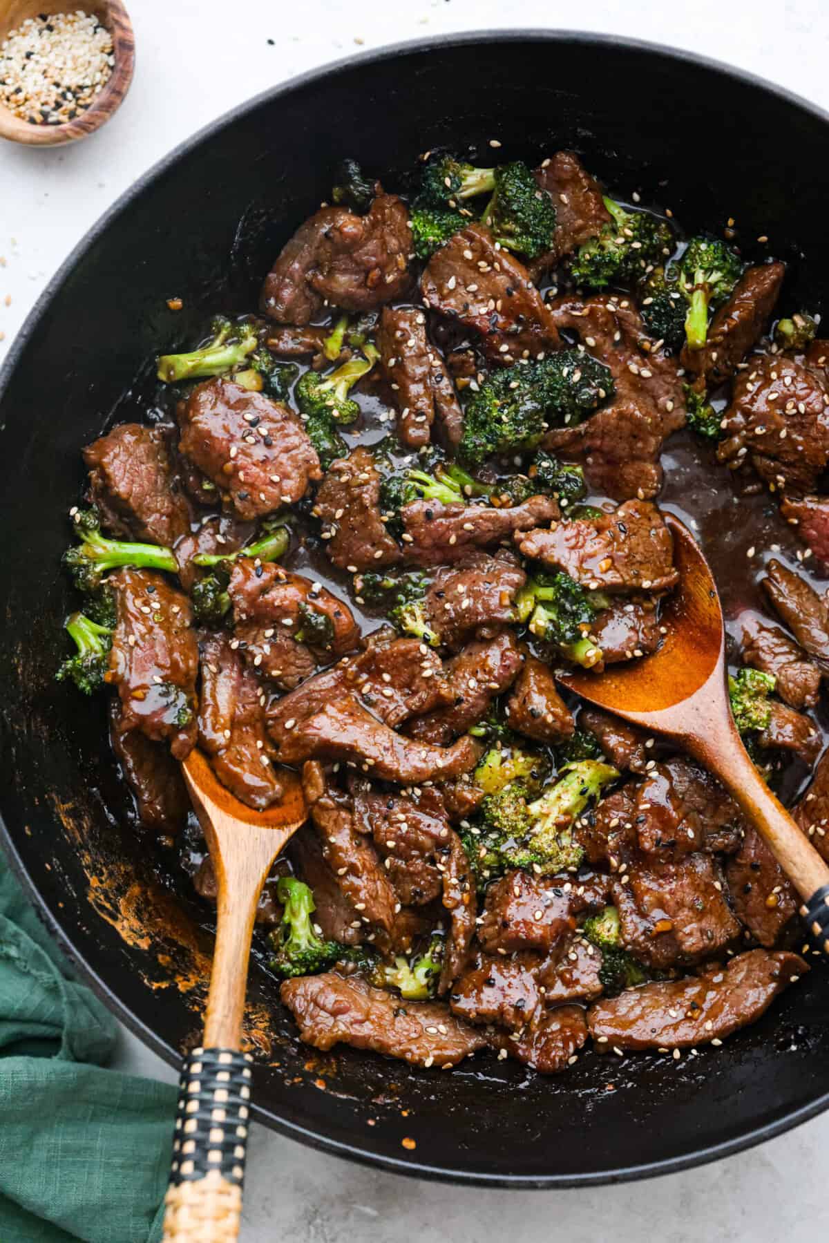 Overhead shot of Mongolian beef and broccoli in a skillet with wooden serving spoons. 