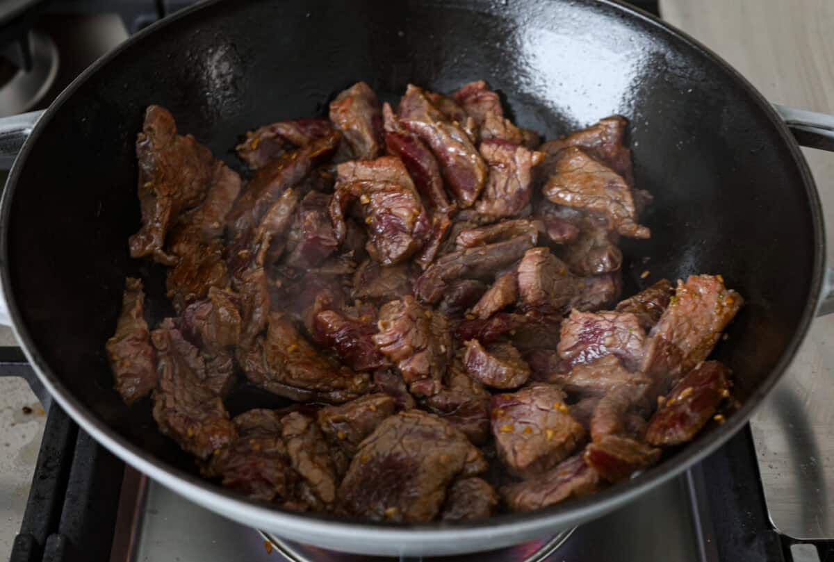 Overhead shot of flank steak sautéing in a skillet. 