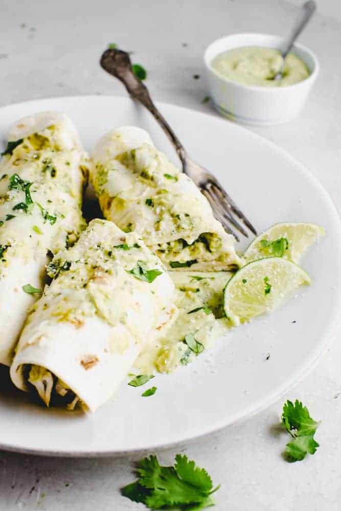 Chicken enchiladas on a plate with lime wedges on the side.