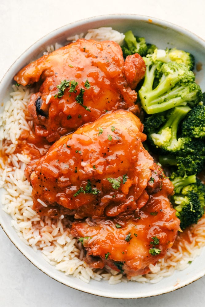 Top-down view of apricot chicken served with rice and broccoli on a white plate.