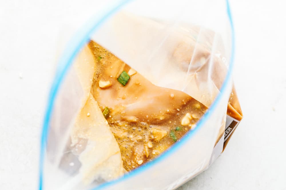 An open ziplock bag with marinade in it and chicken breasts. 