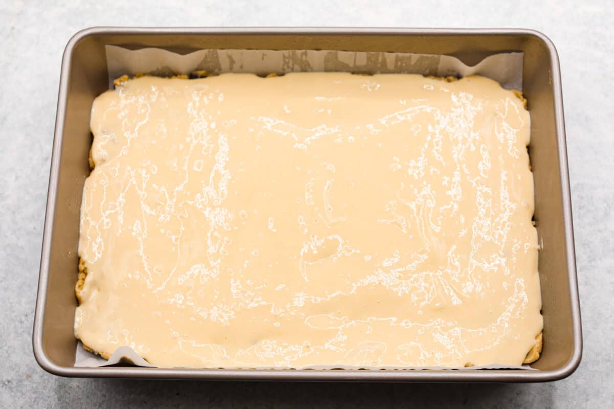 Overhead shot of cheesecake mixture poured on top of the brownie pressed in a pan. 