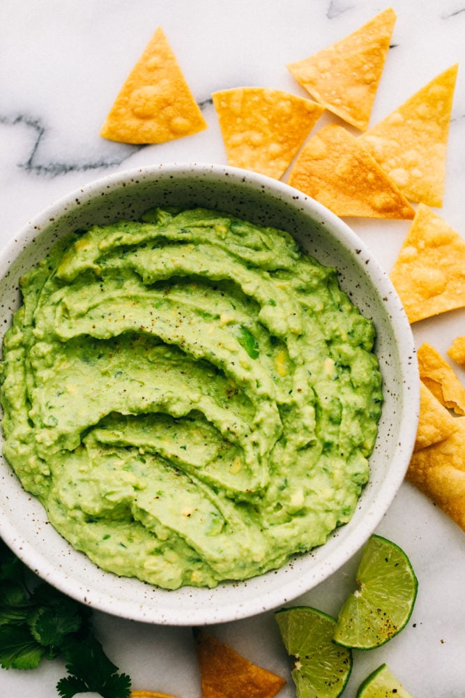 creamy avocado dip in a bowl with chips and lime slices around the edges.
