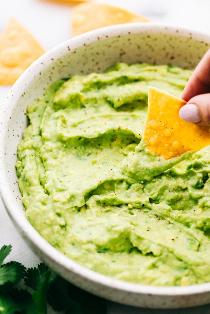 Creamy avocado dip in a bowl with a chip being dipped in and having a little bit of avocado yogurt dip on a chip. 