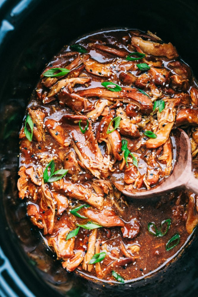 Slow cooker honey garlic chicken in a slow cooker with a wooden spoon stirring it up.