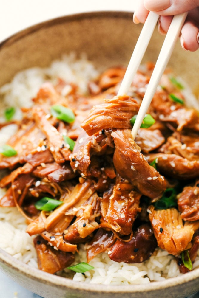 Honey garlic chicken in a bowl with rice underneath and chopsticks picking up the chicken. 