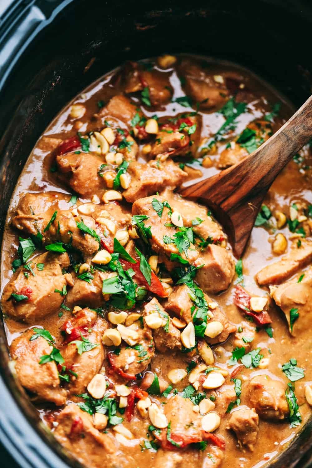 Slow Cooker Thai Peanut Chicken being stirred by a wooden spoon in a pot.