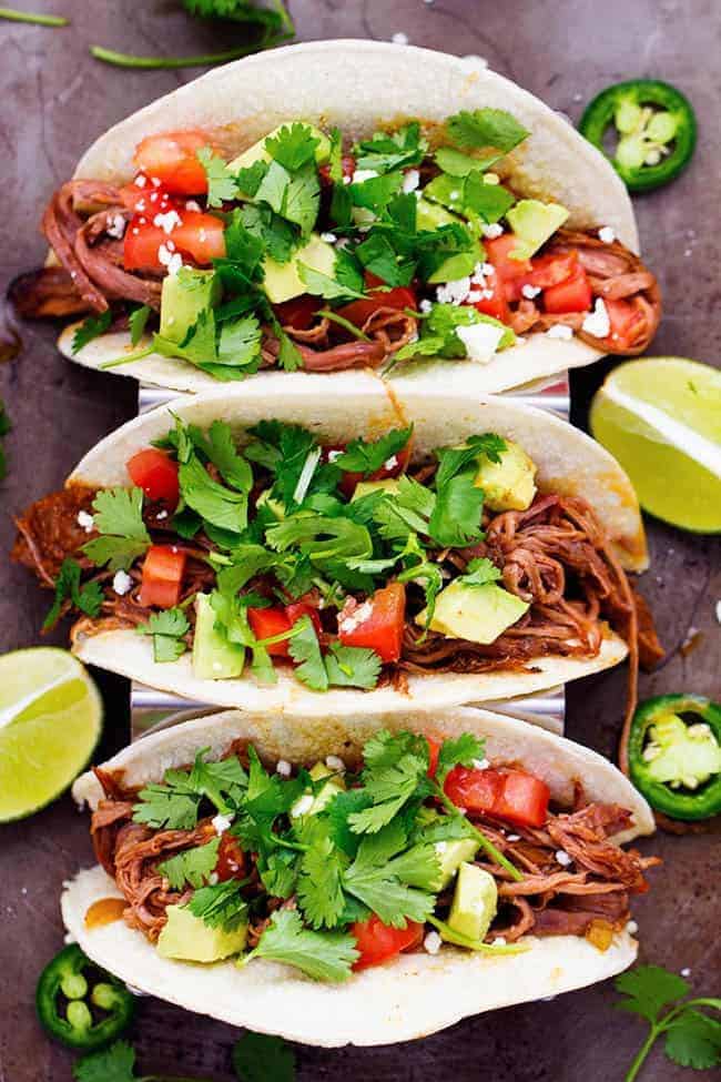 Slow cooker beef tacos with cilantro garnished on top with limes on the side. 