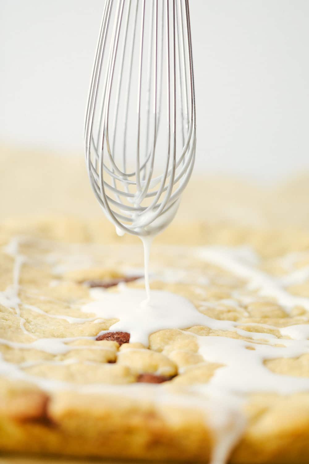 Barras Snickerdoodle horneadas con un batidor rociando sobre un glaseado. 