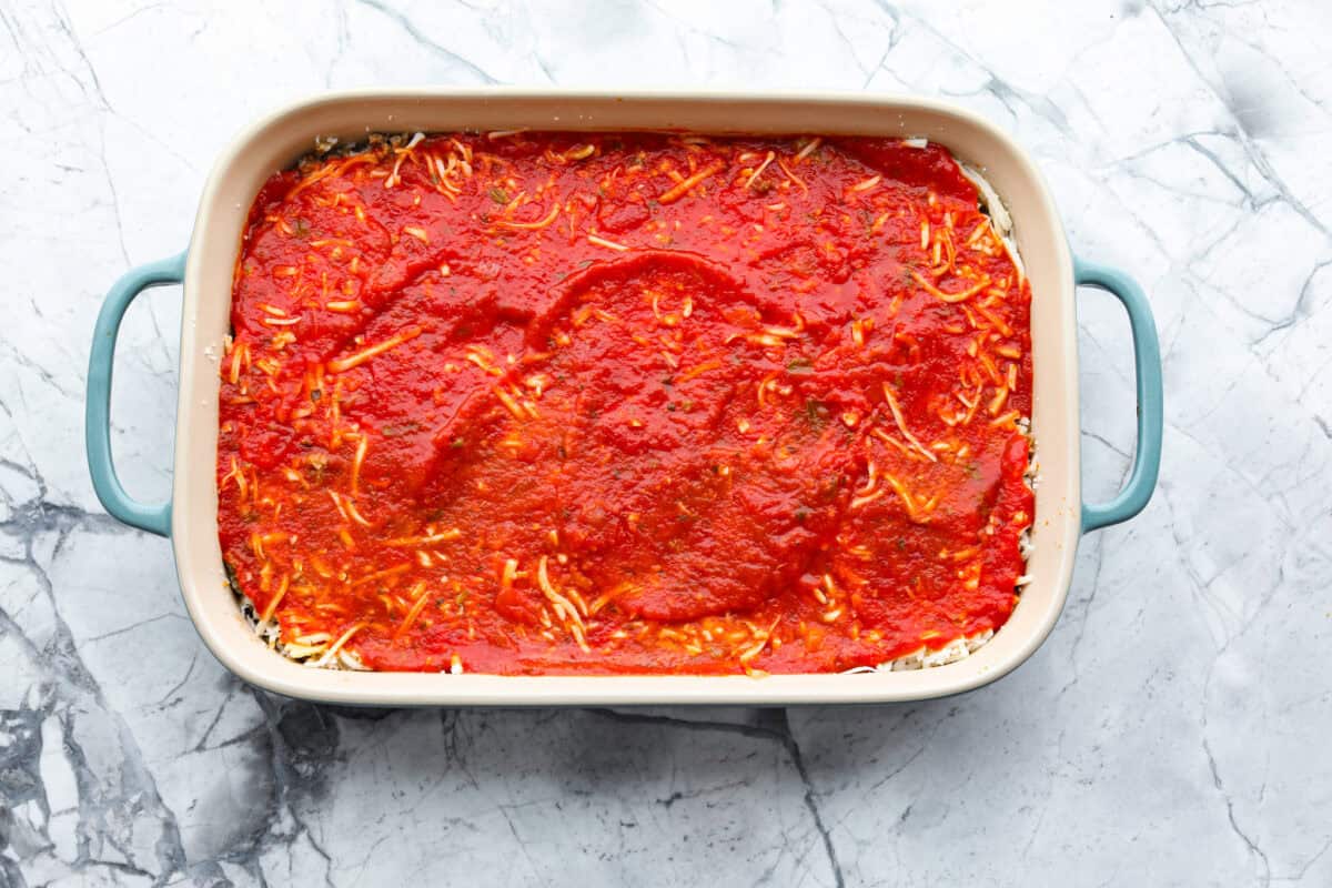 Overhead shot of baking dish with pizza casserole layers up until the pizza sauce. 