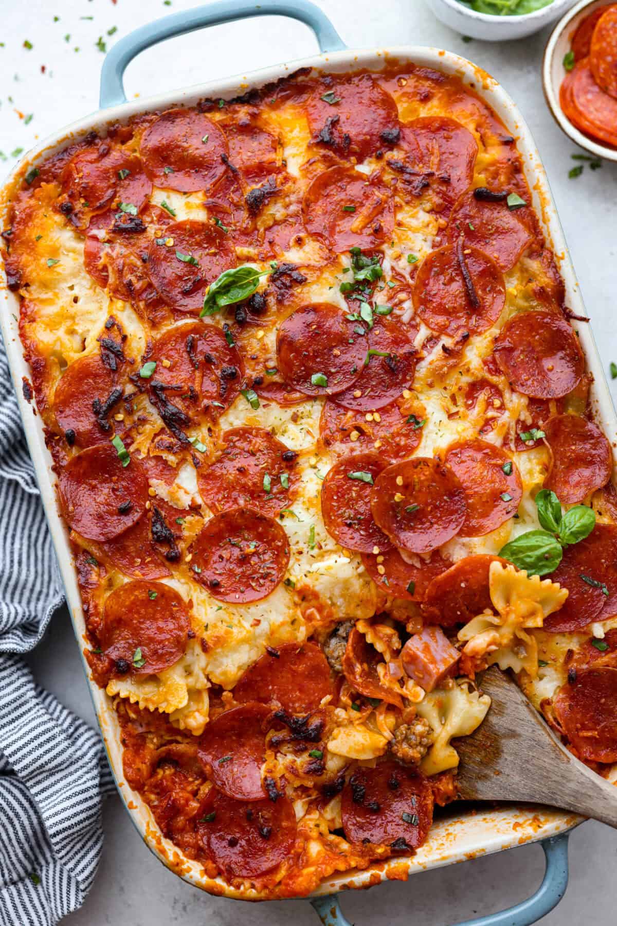 Overhead shot of cooked pizza casserole with wooden spoon inserted into the dish. 