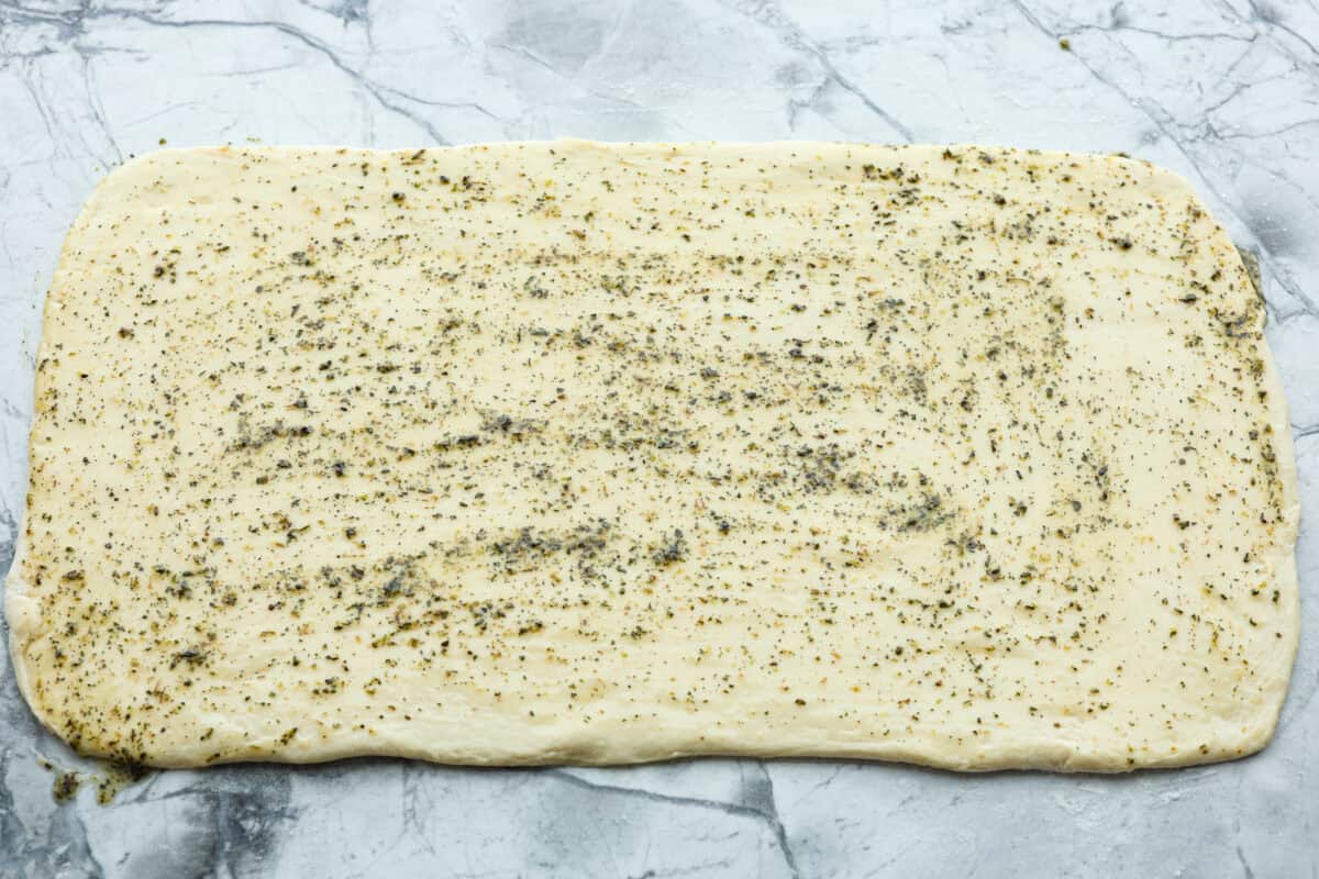 Overhead shot of bread dough rolled out in a large rectangle with garlic butter spread over the top. 