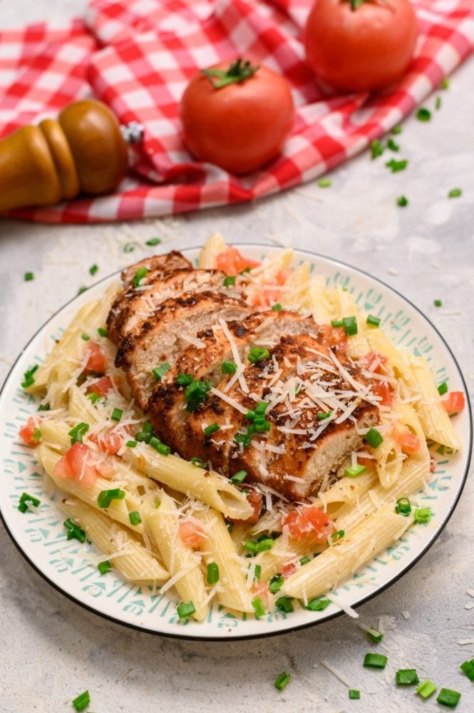 Cajun chicken pasta on a white plate with two tomatoes in the background. 