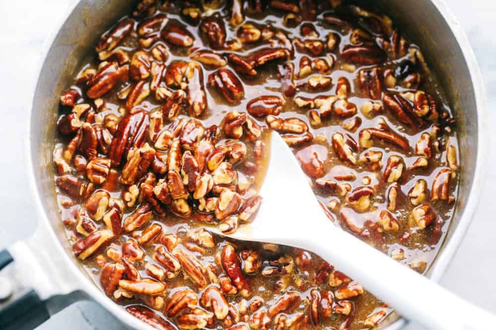 Pecan mixture in a large bowl with a stirring spoon. 