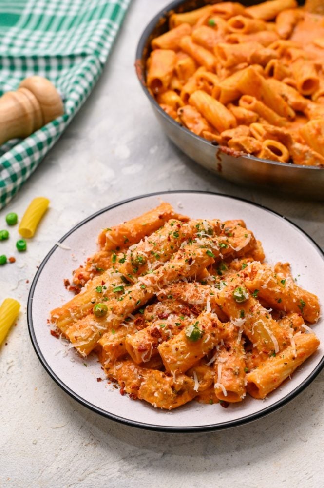 Spicy chicken rigatoni on a white dish with the skillet behind in the photo. 