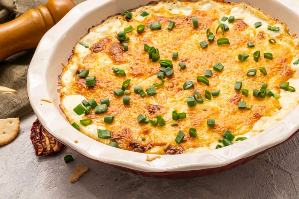 Asiago dip in a white dish with scallions garnished over top. 