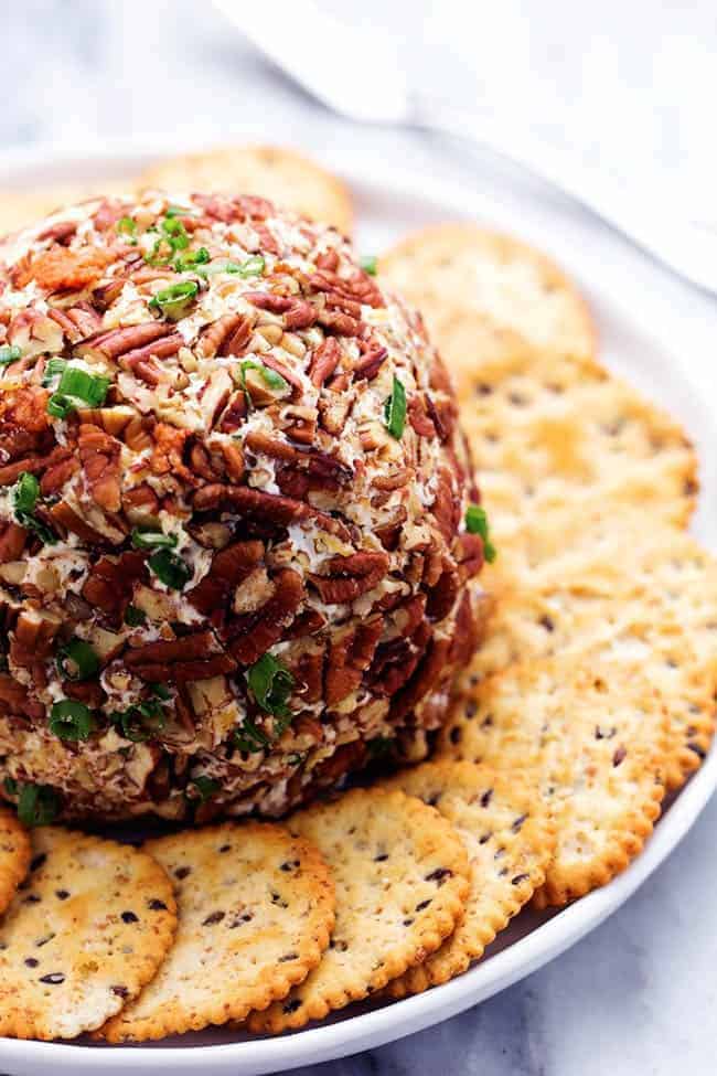 Bacon ranch cheeseball on a white plate with crackers wrapped around the plate and cheeseball. 
