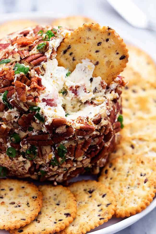 Bacon ranch cheeseball on a plate with crackers wrapped around and a cracker dipped in the cheeseball. 
