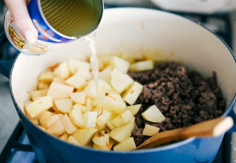 Papas, carne molida y vegetales en una olla con caldo de pollo se vierte sobre ella. 