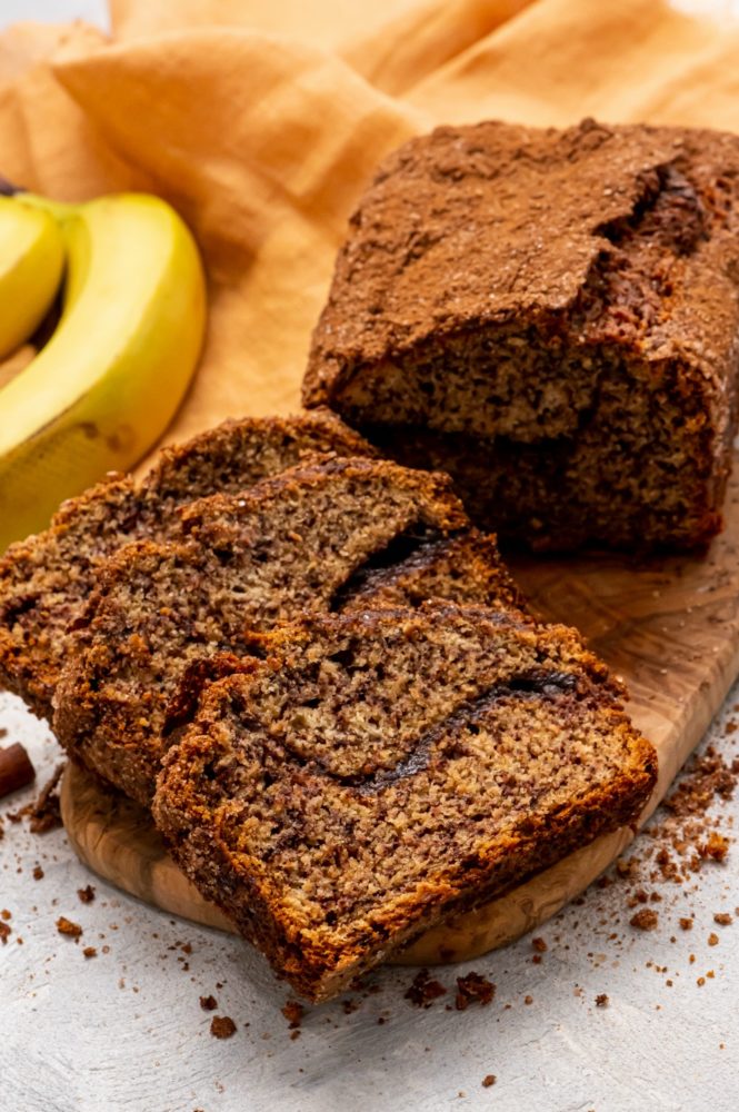 Cinnamon swirl banana bread cut into slices with bananas in the background. 