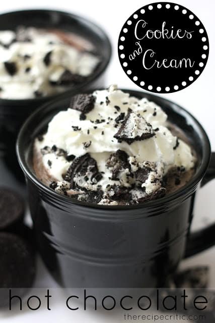 Cookies and cream hot chocolate in black mugs topped with whipped cream and crushed Oreos.