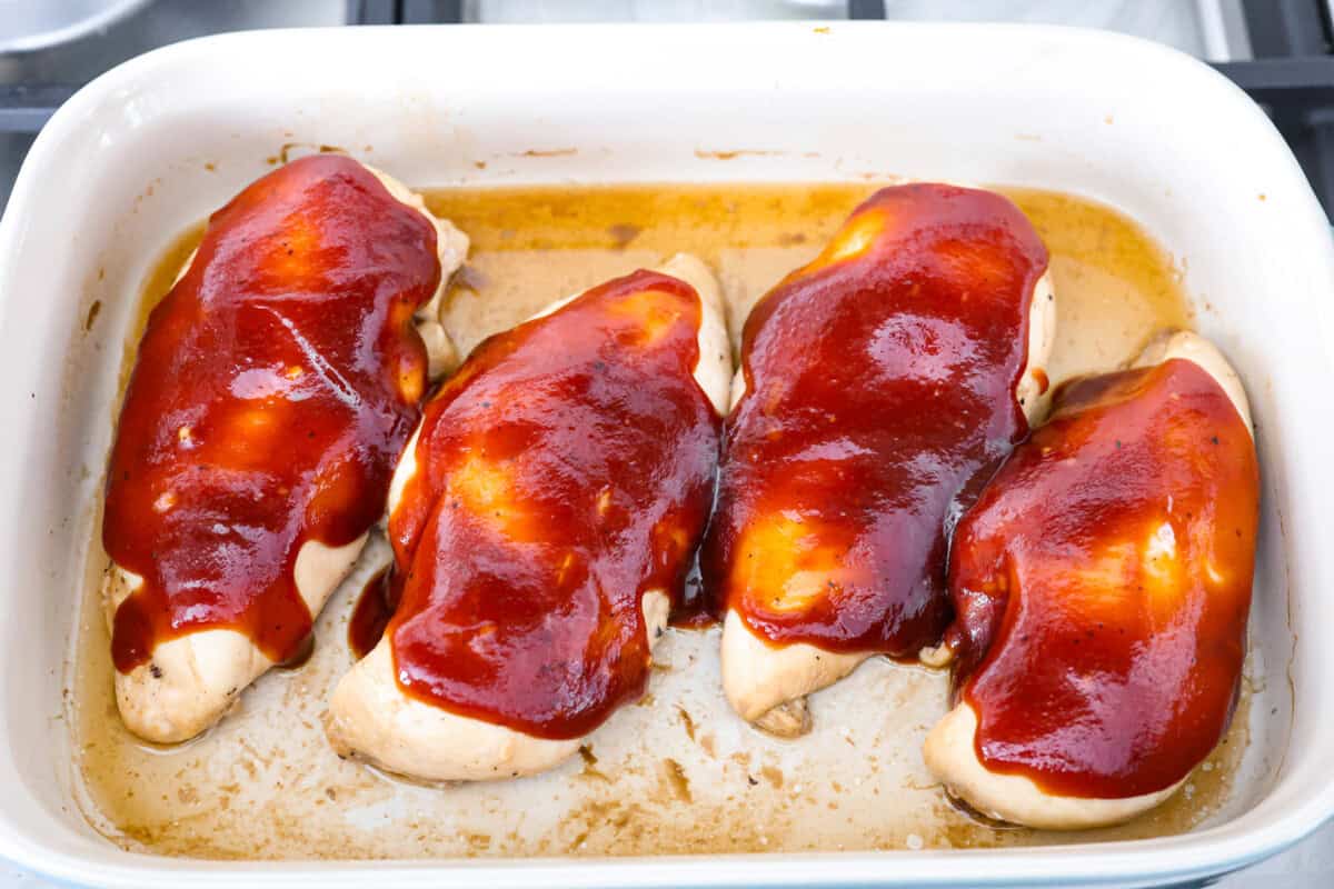 Overhead shot of cooked chicken in a baking dish with BBQ sauce spread on top. 