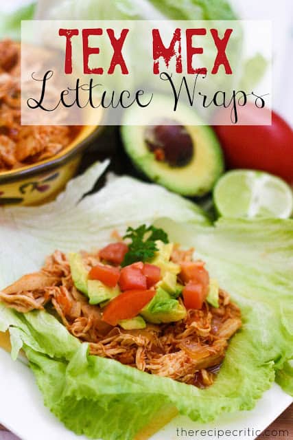 Tex Mex Lettuce wrap garnished with avocado, tomato, and cilantro with a blue and white bowl beside it with extra meat. An avocado, lime, and tomato are sitting beside the wrap.