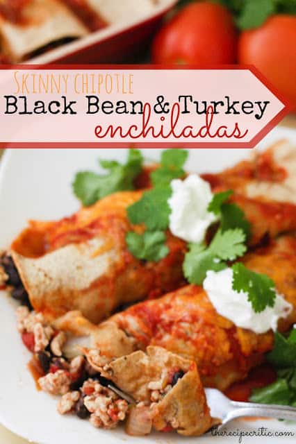 2 black bean and turkey enchiladas lay on a white plate garnished with cilantro and sour cream.