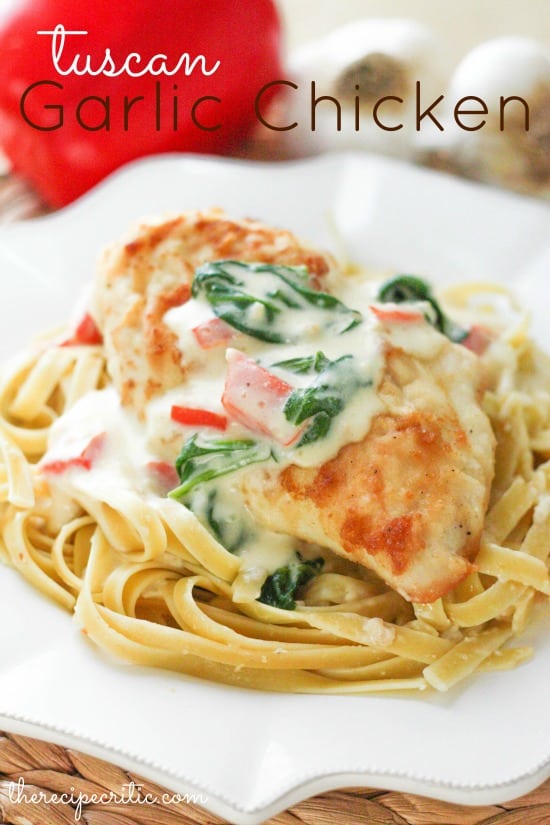 Tuscan garlic chicken on top of noodles and drizzled with a white sauce and spinach and tomatoes all on a white plate.