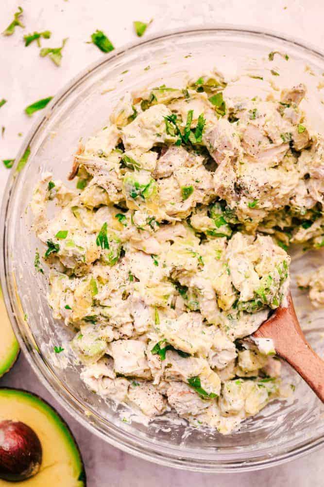 Avocado Chicken Salad in a clear bowl with a wooden spoon. 