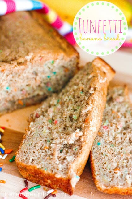 A loaf of funfetti banana bread with 2 slices cut off laying beside it on a wooden board.