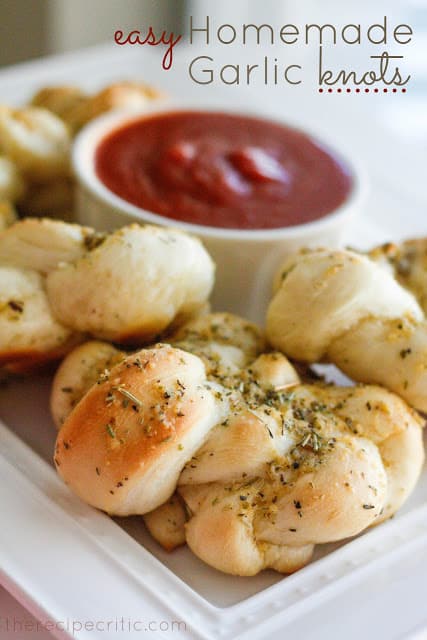Easy homemade garlic knots on a white plate with a bowl of marinara sauce in the center of the plate.