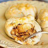 3 chicken enchilada puffs on a tan plate. One has a bite missing and a fork in it.