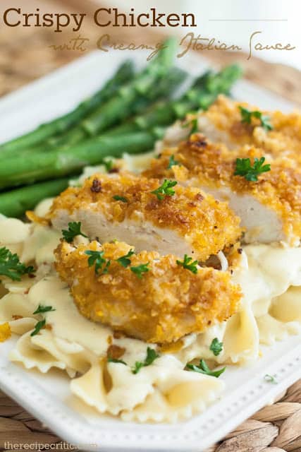 Crispy chicken with creamy italian sauce on a white plate with pasta and asparagus.