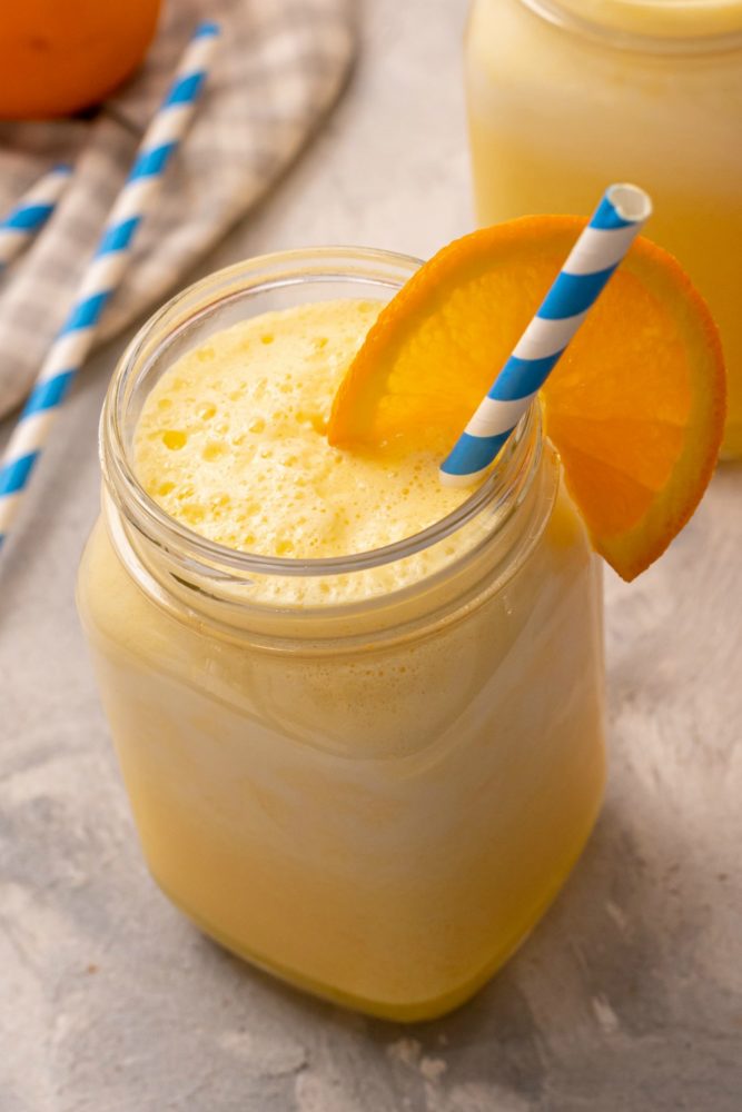 Orange Julius drink in a glass mason jar garnished with an orange and striped straw.