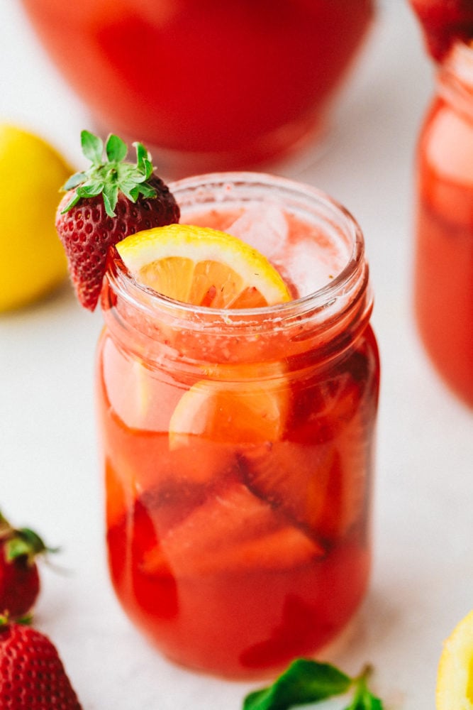 Erdbeerlimonade in einem Einmachglas, garniert mit weiteren frischen Erdbeeren, einer Zitronenscheibe und einem Erdbeerstück als Beilage.