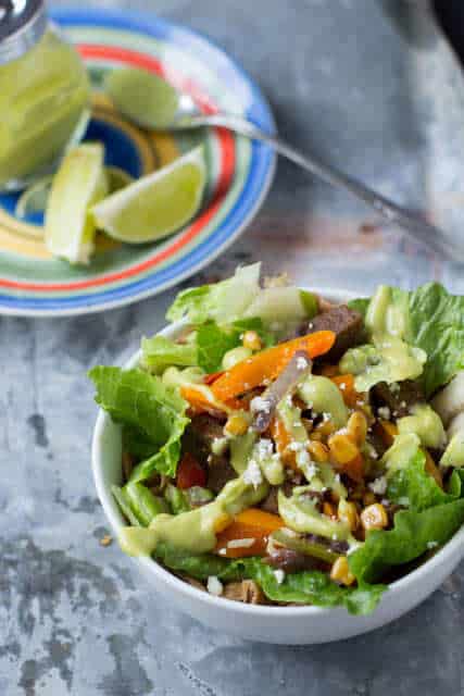 Steak Fajita salad in a white bowl beside a plate of lime slices.